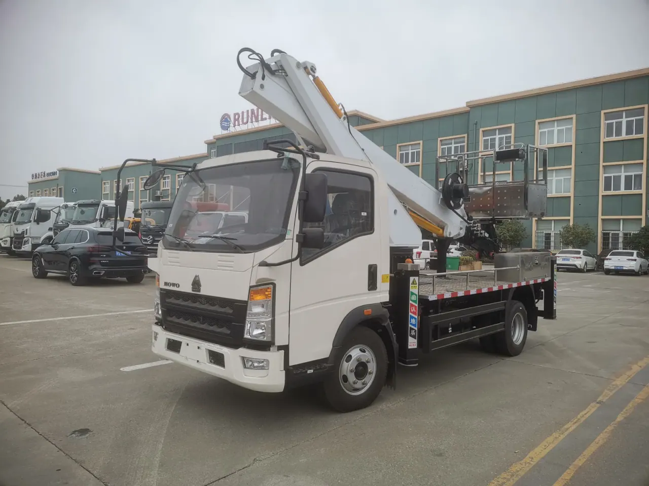 Front-side view of a white HOWO truck with its aerial boom folded above the cab