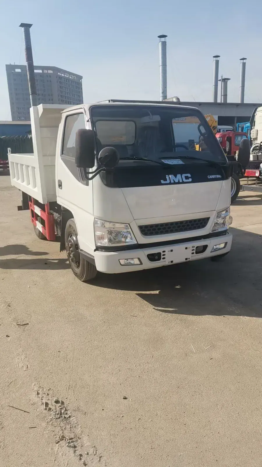 Front view of a compact white JMC dump truck in a vehicle yard