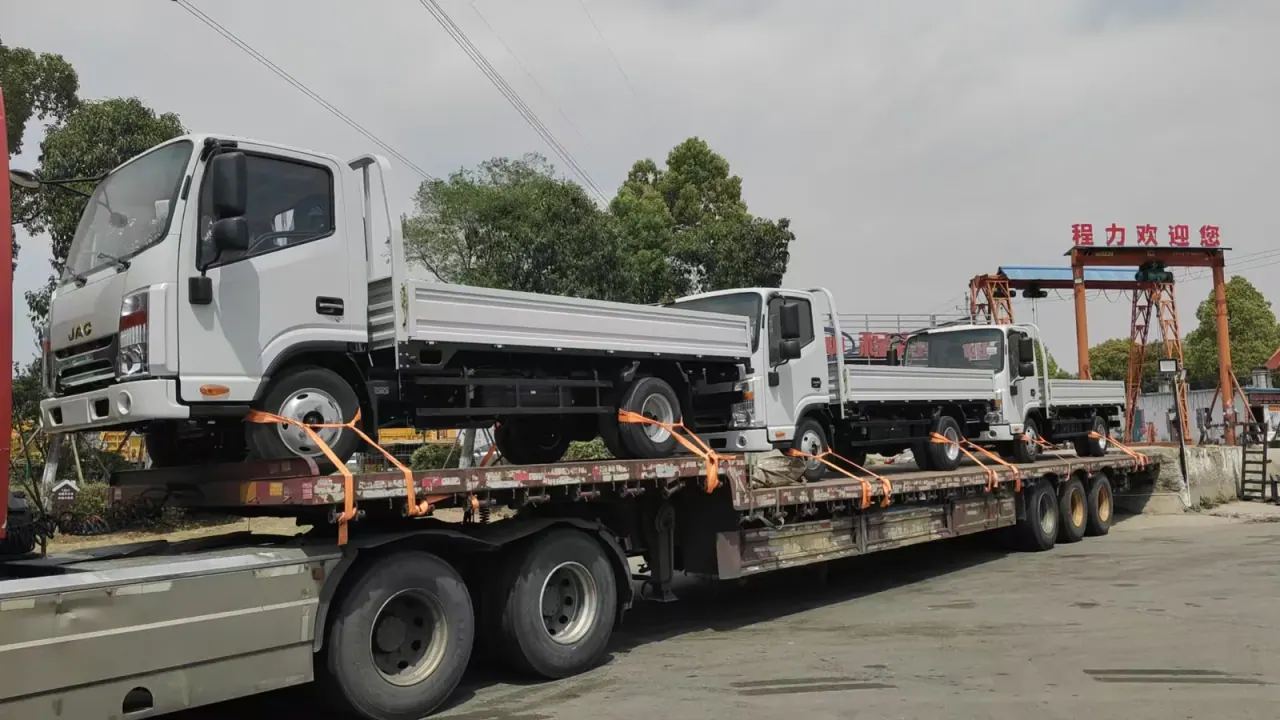 JAC drop-side truck secured by straps on a road transport platform