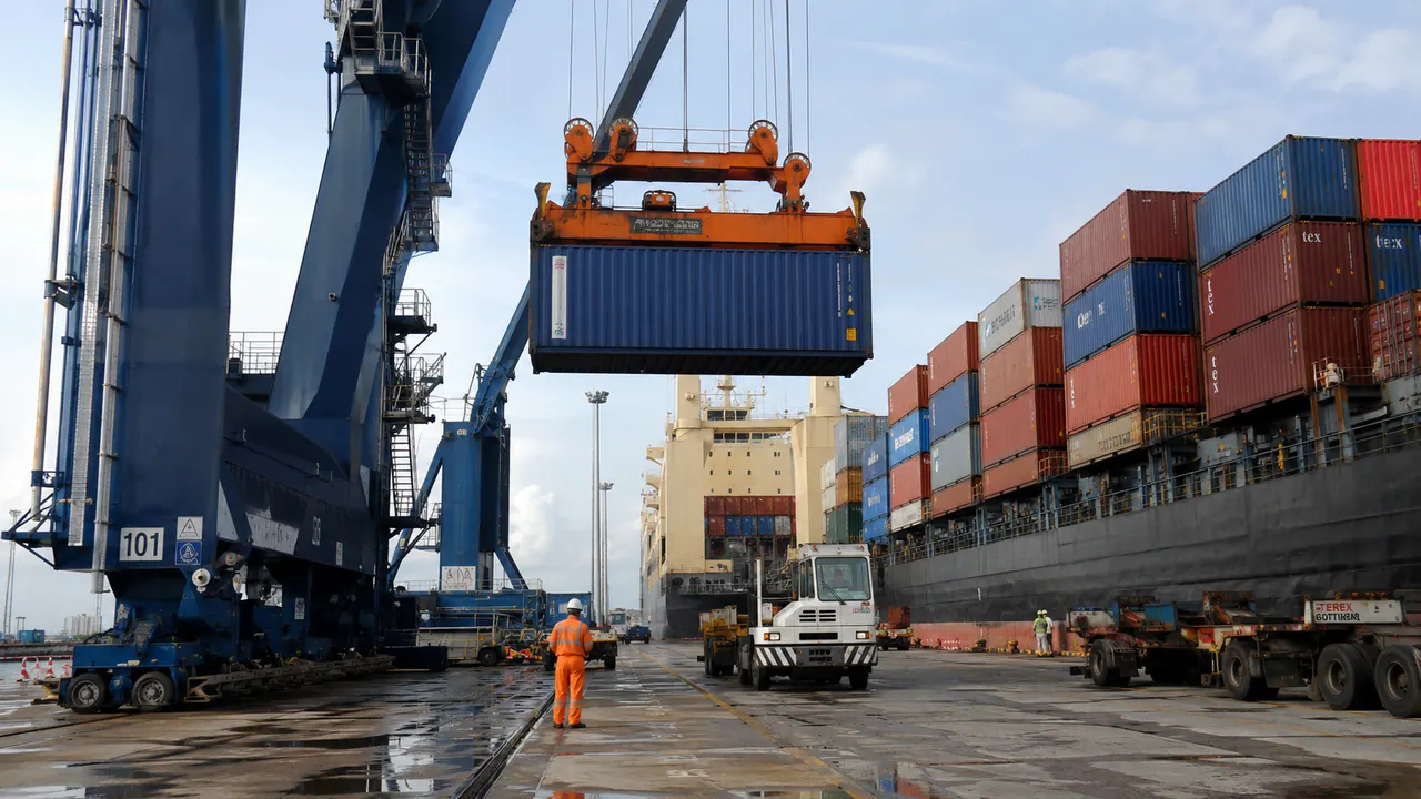 A shipping container being lifted beside a cargo vessel at a port
