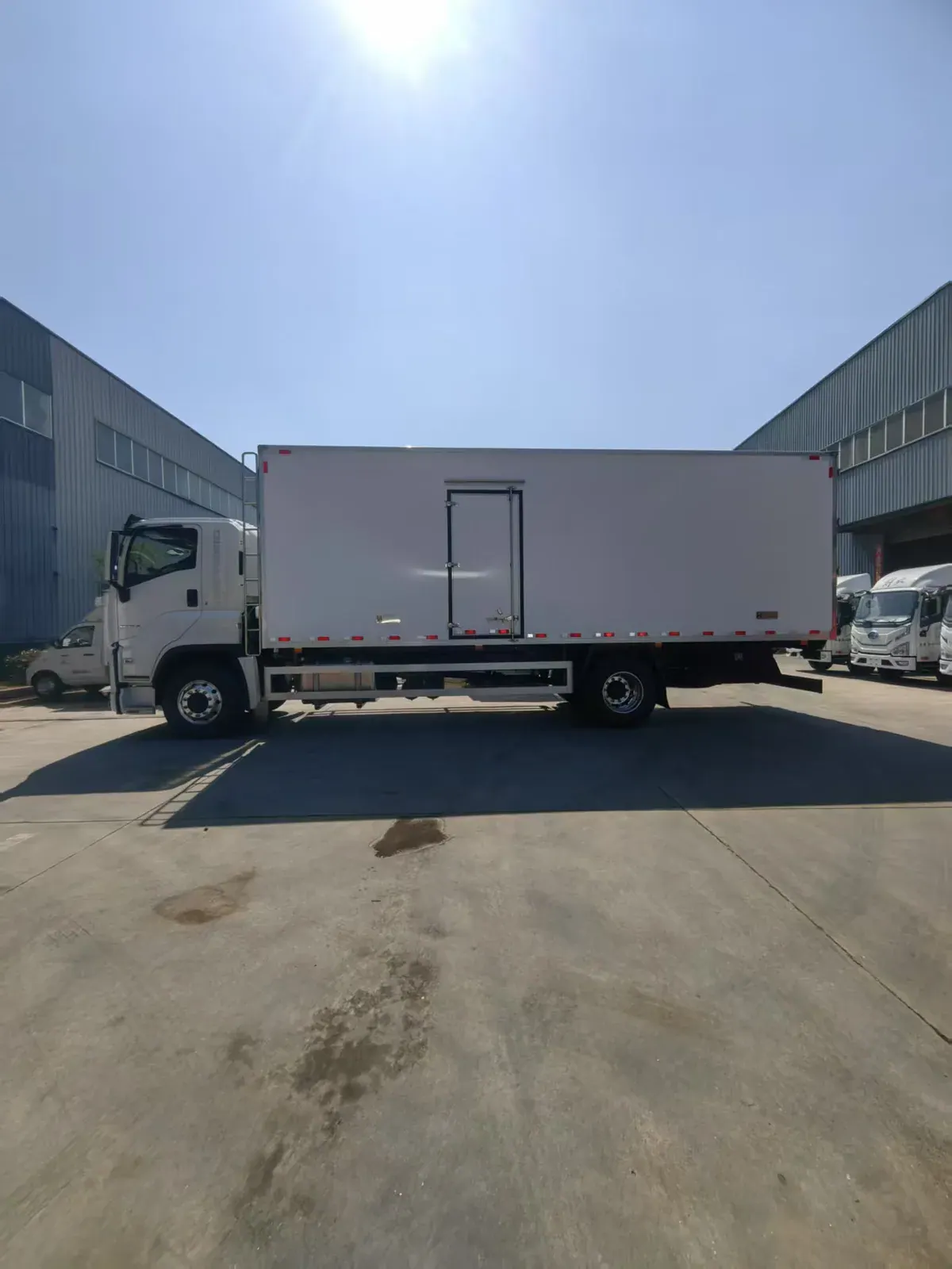 Full side profile of a white ISUZU truck with a long enclosed body and side door